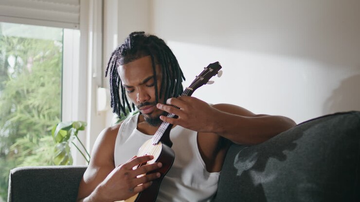 Musicista concentrato che suona la chitarra a casa. Uomo soddisfatto che si gode l'ukulele.