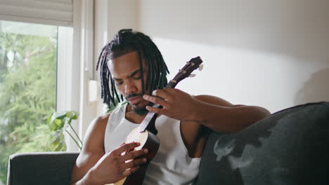 focused musician playing guitar domestic place. satisfied man enjoying ukulele