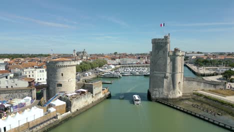 Chain-and-Saint-Nicolas-towers-with-French-flag-waving,-La-Rochelle-old-port-in-France