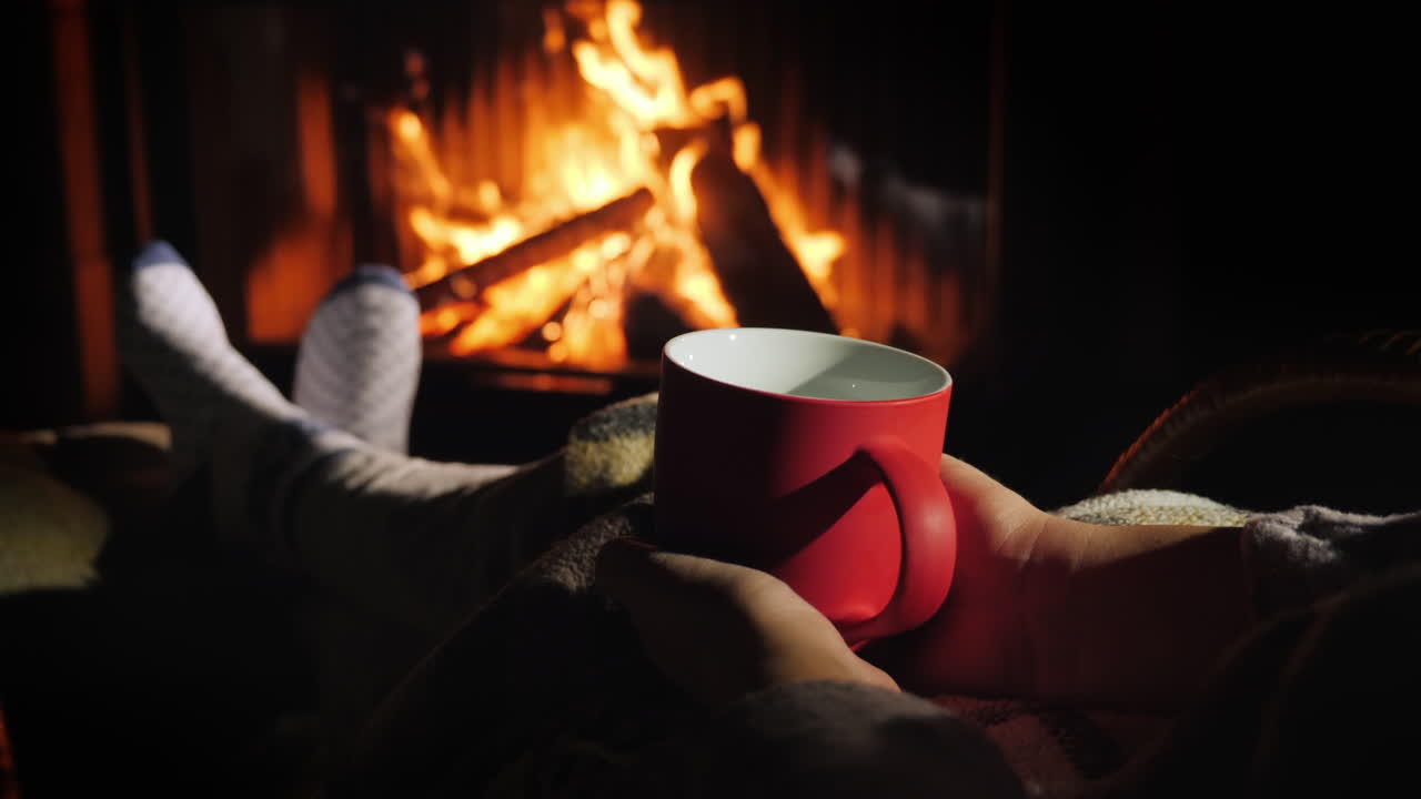 빨간 차 한 잔을 든 여자가 벽난로 옆에서 휴식을 취하고 있다