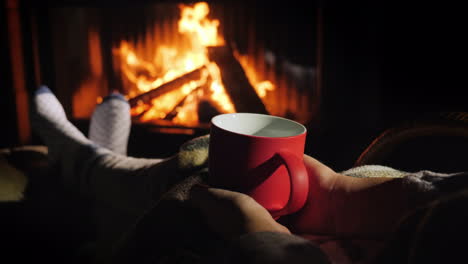 woman with a red cup of tea is relaxing by the fireplace