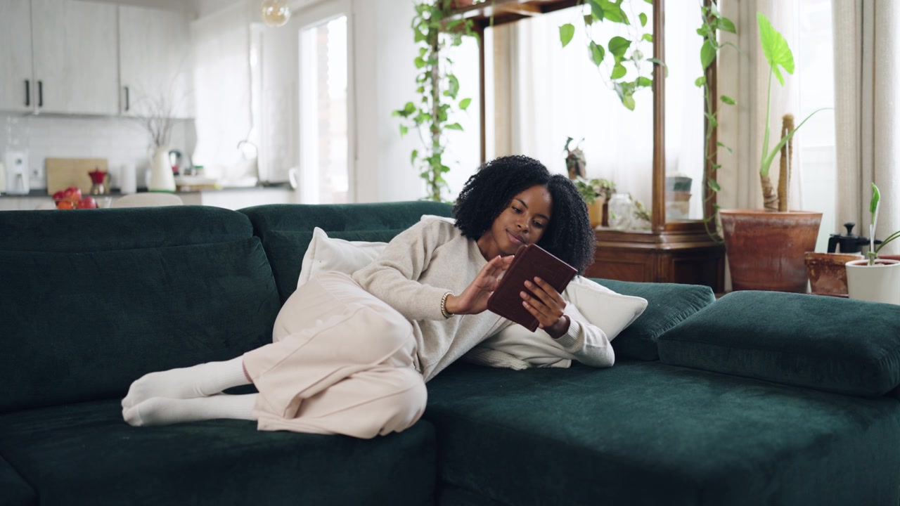 Young African American Woman Relaxing on Sofa Using Tablet