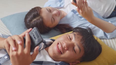 close up of asian teen couple playing smartphone while lying on carpet on the floor at home. phone addicted couple