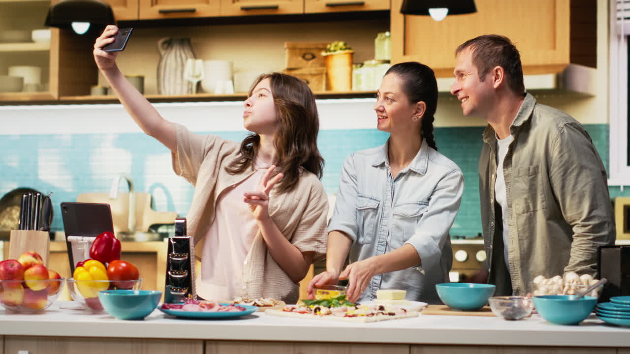 Pre-teen daughter taking pictures of her and parents preparing pizza together
