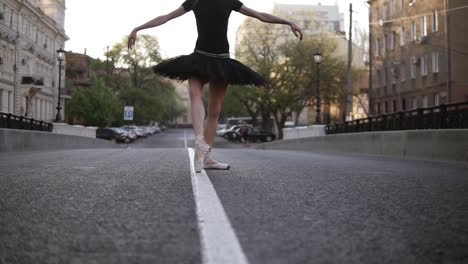 ballerina in black ballet tutu and point on empty street in the middle of the road. summer morning. young beautiful woman practicing ballet movements and exercises. close up. no face