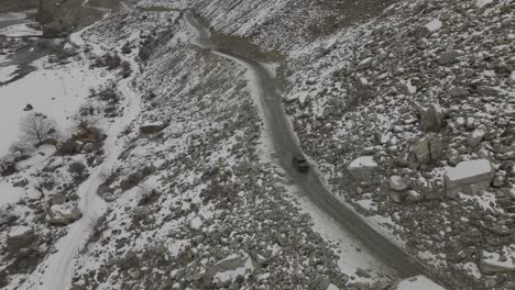 aerial view of black truck driving along road through snow covered rocky landscape of hunza valley