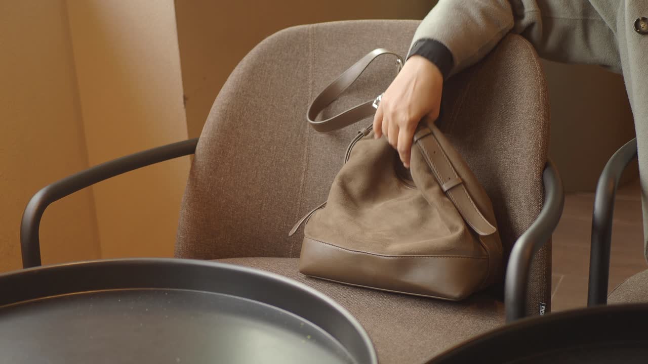 Persona che prende una borsa a mano in pelle scamosciata marrone da una sedia