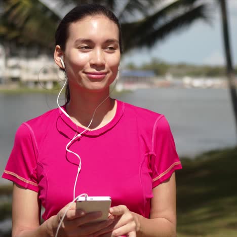 Mujer-Casual-Escuchando-Música-En-El-Teléfono-Inteligente-En-La-Orilla-Del-Lago