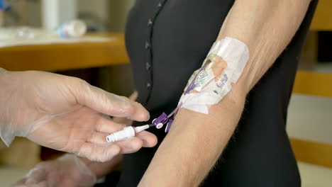 enfermera médica haciendo una visita a un paciente intravenoso en casa usando guantes estériles e inyectando solución salina de una jeringa en una línea picc