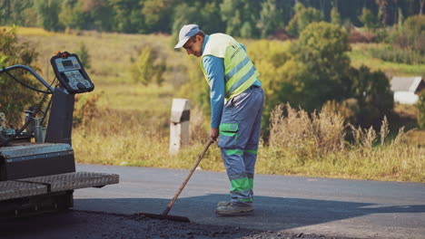 workers make road asphalting on the natural background of trees. male workers in protective uniform are working on one side of the road. new asphalt on the highway.