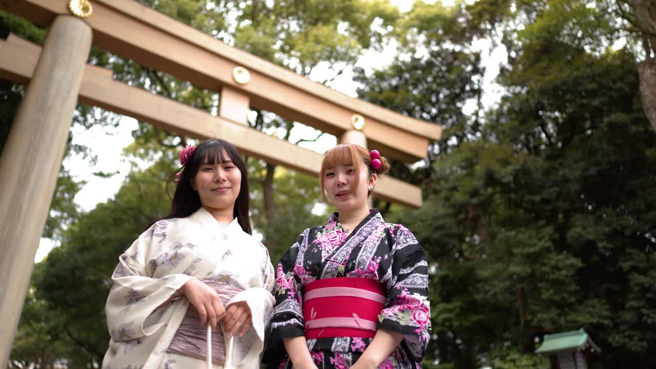Inquadratura dal basso di due amici in kimono in piedi davanti a un cancello torii di legno