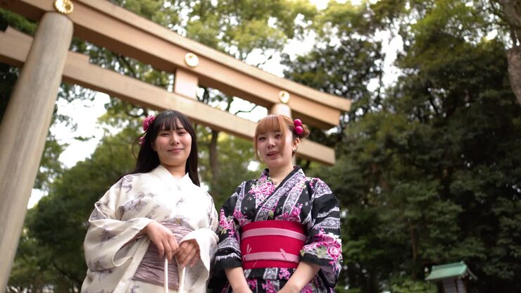 Inquadratura dal basso di due amici in kimono in piedi davanti a un cancello torii di legno