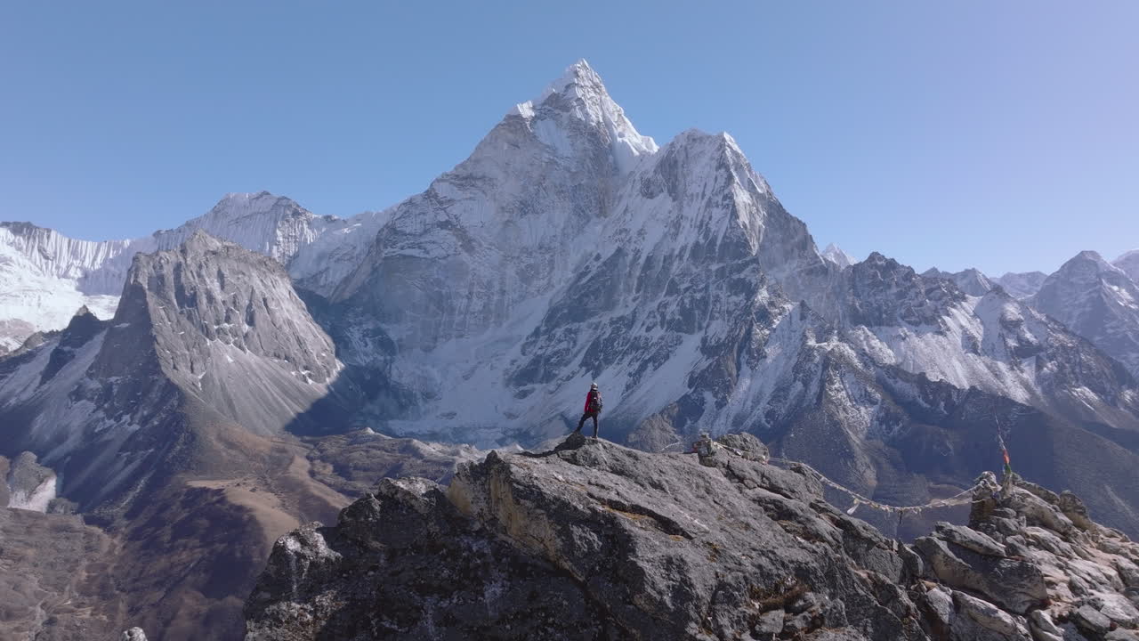 Ripresa aerea con drone in allontanamento che rivela un turista sulla cima del picco Nangkartshang vicino a Dingboche, mentre ammira la vista dell'Ama Dablam e della catena himalayana nella regione dell'Everest in Nepal.