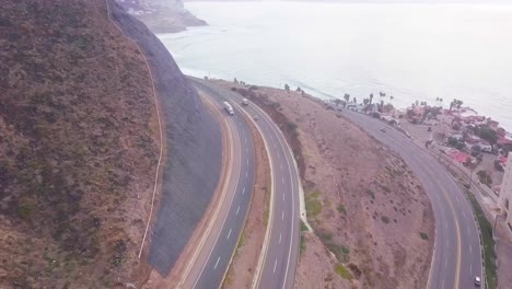 Blick-Von-Einer-Drohne,-Die-In-Einer-Kurve-über-Die-Straße-Fliegt-Und-Den-Blick-Auf-Das-Meer-Von-Rosarito-In-Mexiko-Freigibt