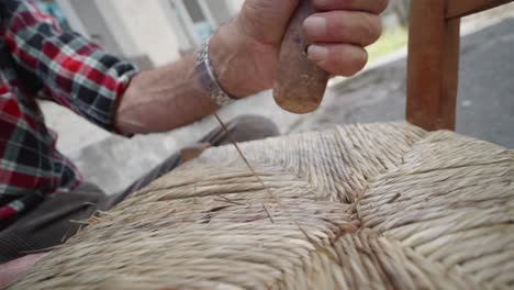 una vista más cercana sobre un momento de tejido de sillas con un fabricante de sillas de mimbre haciéndolo, italia.