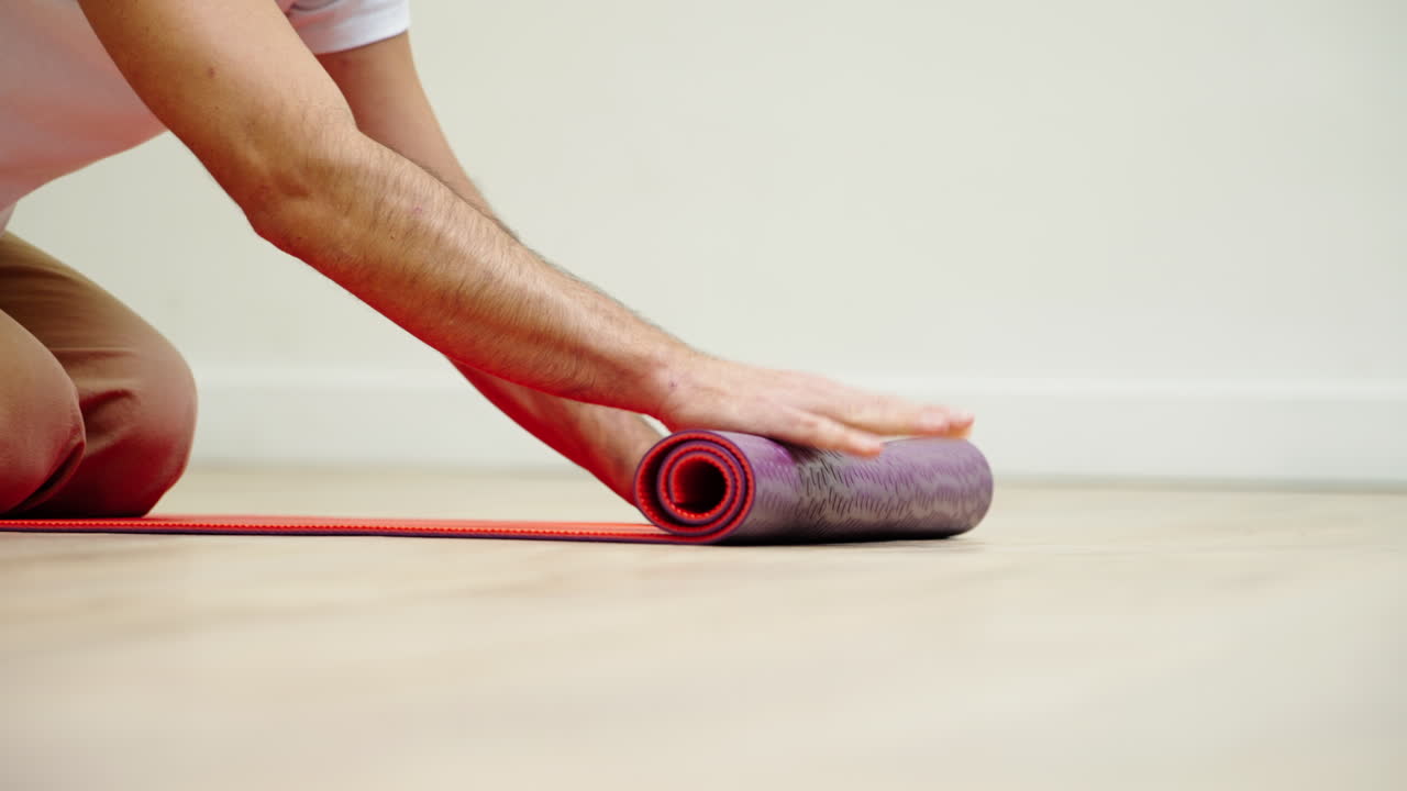 Uomo che arrotola il tappetino da yoga su pavimento in legno