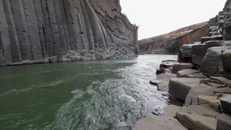 Rushing-river-flows-through-a-dramatic-basalt-column-canyon-in-Iceland,-showcasing-nature's-raw-beauty-and-geological-wonder