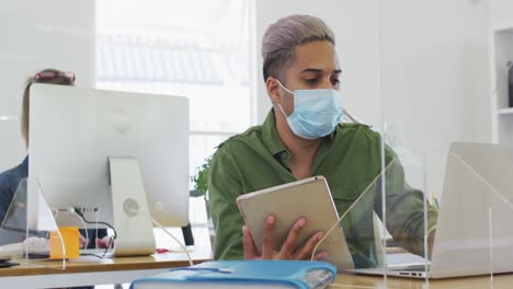 hombre con una máscara facial usando una computadora portátil y una tableta digital en la oficina