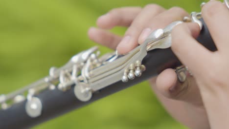 close up of a man's fingers playing a clarinet with green blurred background