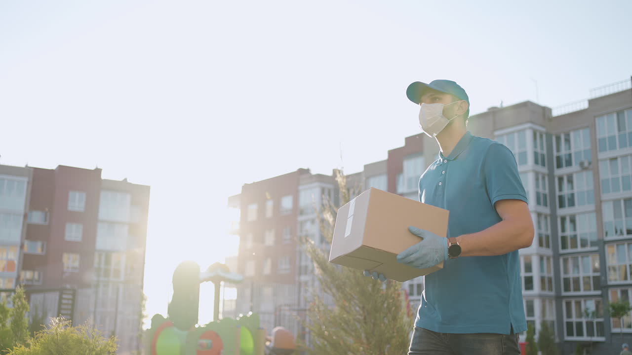 The male deliveryman in masks and protective gloves carries a parcel to the customer with a terminal for contactless payment by mobile phone or NFC card.