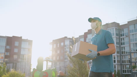 el repartidor masculino con máscaras y guantes de protección lleva un paquete al cliente con una terminal para el pago sin contacto por teléfono móvil o tarjeta nfc.