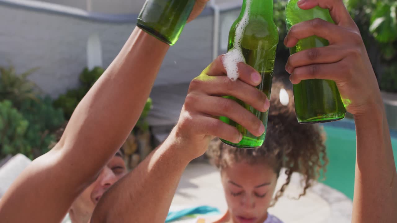 diversos amigos masculinos y femeninos felices haciendo brindis con botellas de cerveza en la fiesta de la piscina