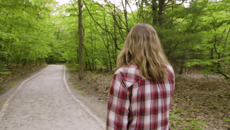 Handheld-shot-following-a-young-woman-walking-down-a-trail-in-the-forest