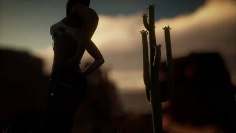 femme en chemise déchirée debout près d'un cactus dans le désert au coucher du soleil