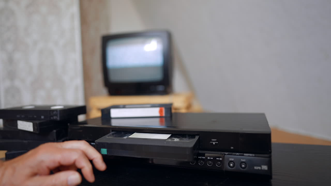 Video Home System working indoors. Male hand puts a DVD tape into the player and it then appears again. Close up