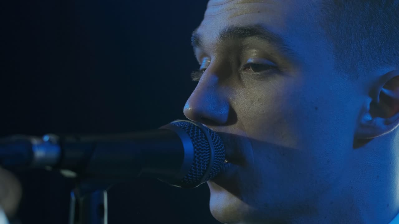 Man singing song in microphone during performance on stage on rock concert. Close up man rock star singer on music concert on colorful light background
