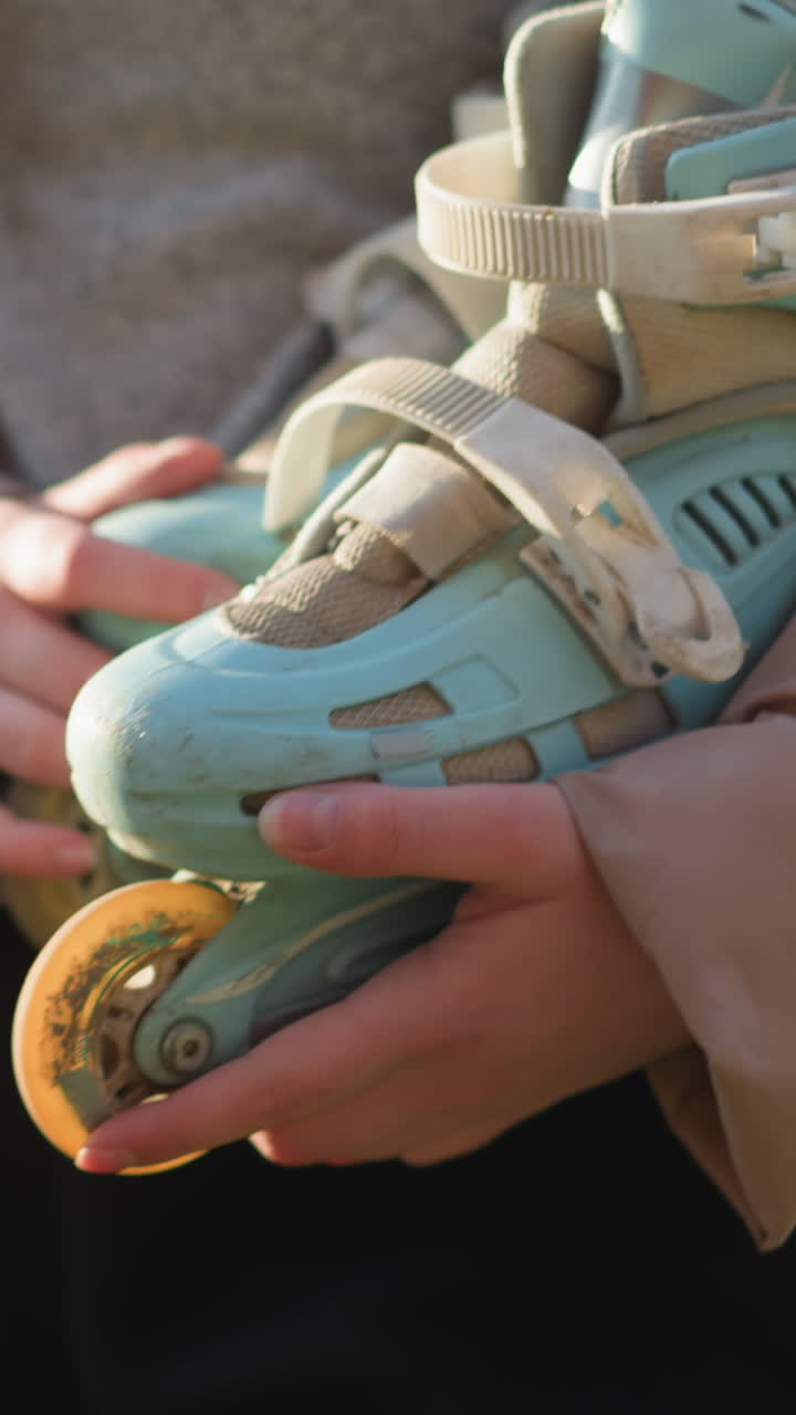 빛이 비치는 공원을 걸어가는 동안 두 손으로 롤러블레이드를 들고 있는 소녀의 클로즈업. 그녀는 복아색 재을 입고 있으며 빛은 따뜻하고 조용한 분위기를 만니다.