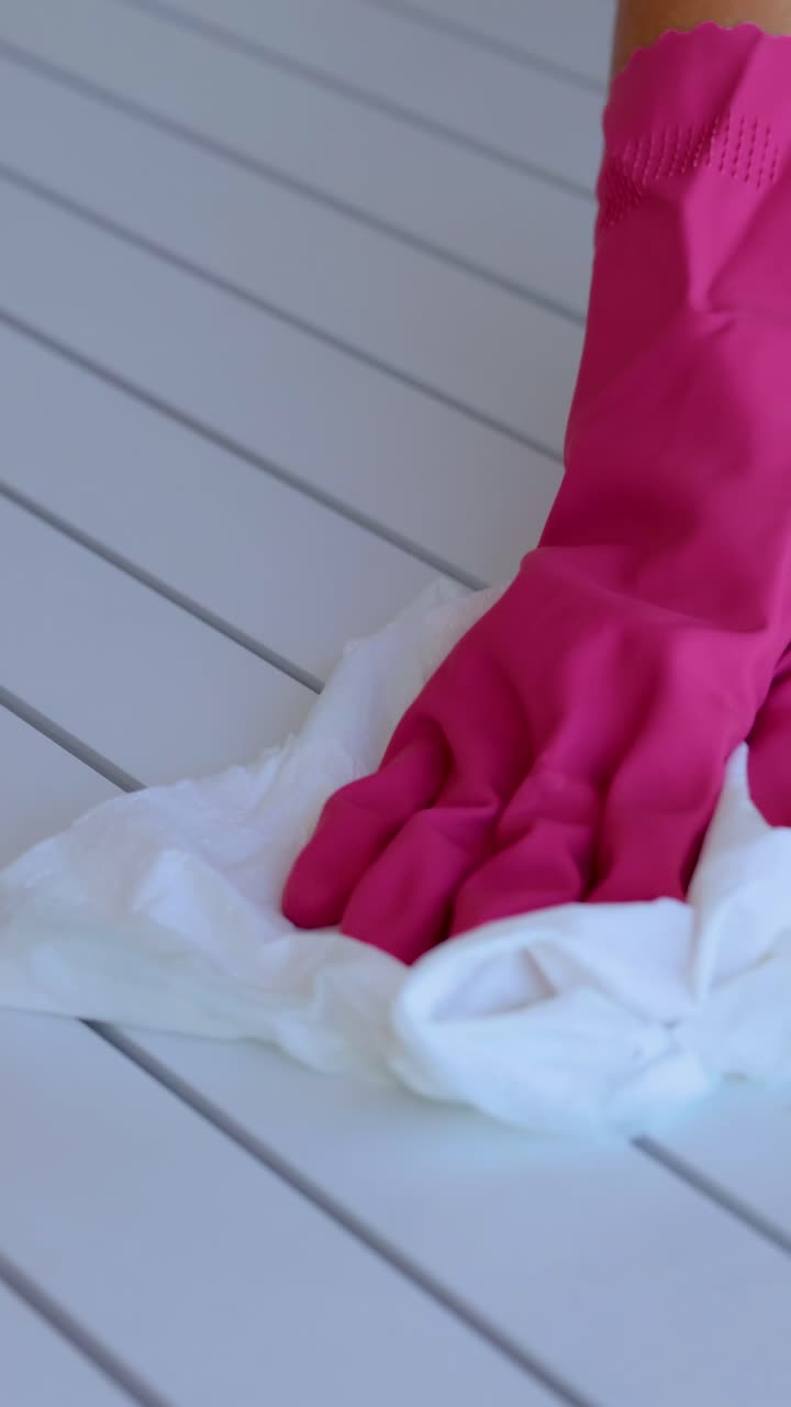 Pink-gloved hands wipe a white table with a cloth, under bright lighting, showcasing a cleaning process