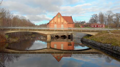 Drohnenaufnahmen,-Die-Sich-Langsam-Auf-Eine-Kleine-Brücke-Mit-Einem-Wasserkraftwerk-Im-Hintergrund-Zubewegen