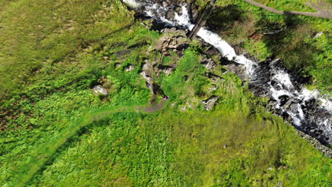 Descending-drone-footage-of-two-people-in-remote-vivid-green-countryside-with-fast-flowing-river