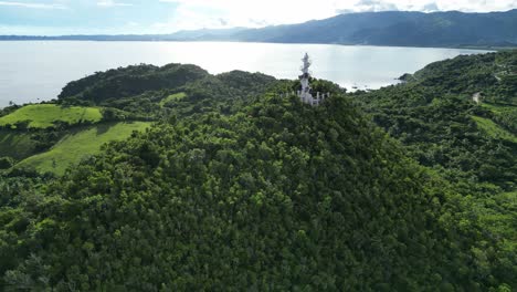 cinematic birdseye aerial view of white bote lighthouse atop jungle-covered mountains with pristine island background of the calm ocean bay and rainforest