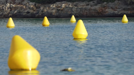 group of six yellow conical navigation buoys indicating a path for boats in a rocky cove