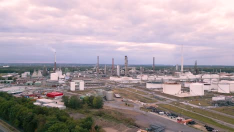 Aerial-drone-fly-away-from-an-chemical-industry-plant-in-Sürth,-Cologne,-Germany---plant-producing-fuel-gas-for-transportation-with-chimneys-and-cloudy-sky---bird-view-helicopter-flight-summer-2022