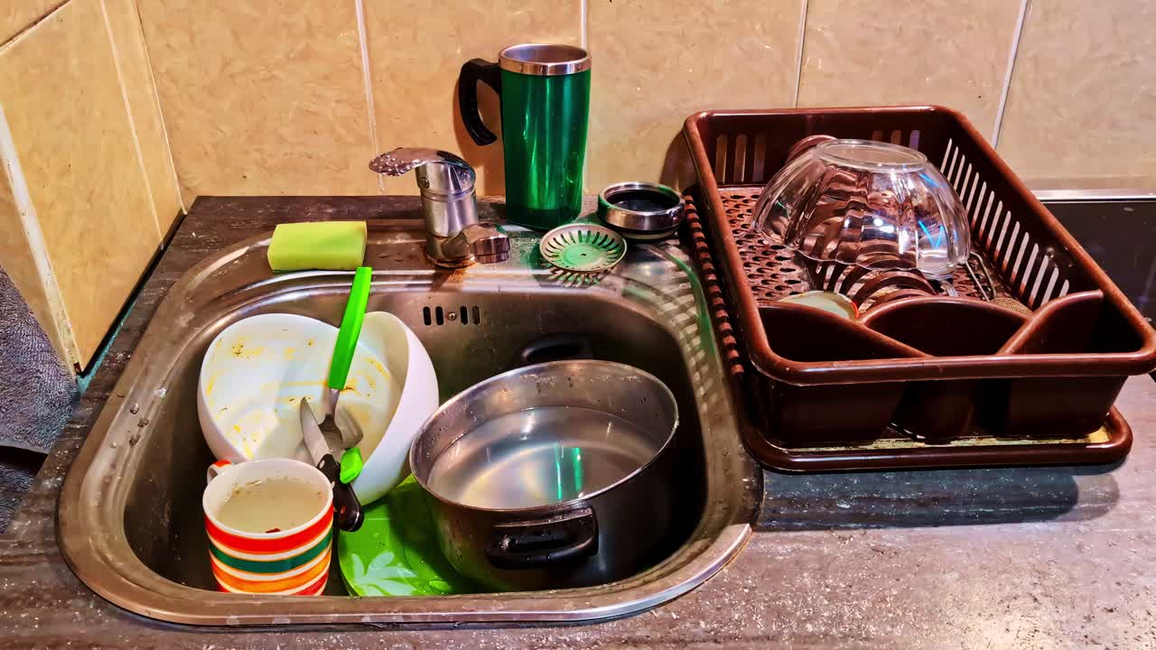 Messy kitchen sink with dishes, cups, and utensils next to drying rack
