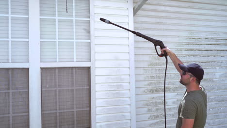 homeowner pressure washes home siding summer day