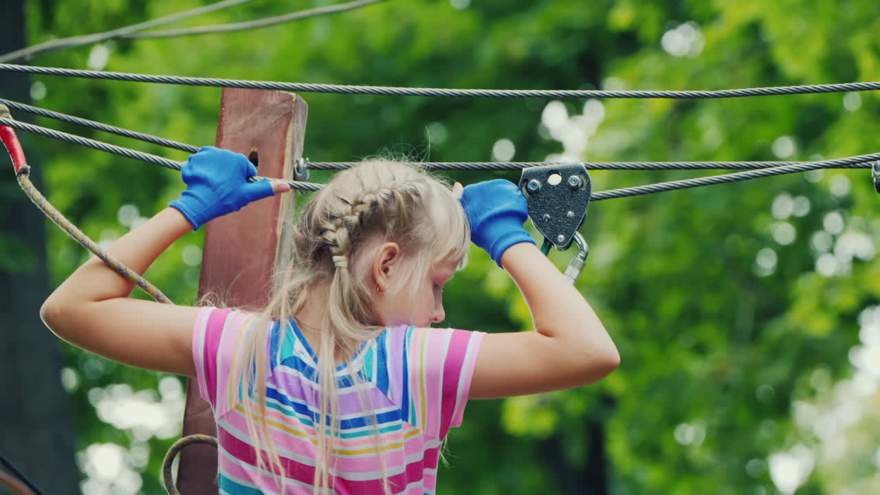 나무 사이의 밧줄을 따라 움직이는 용감한 소녀의 뒷모습은 안전 밧줄을 사용합니다