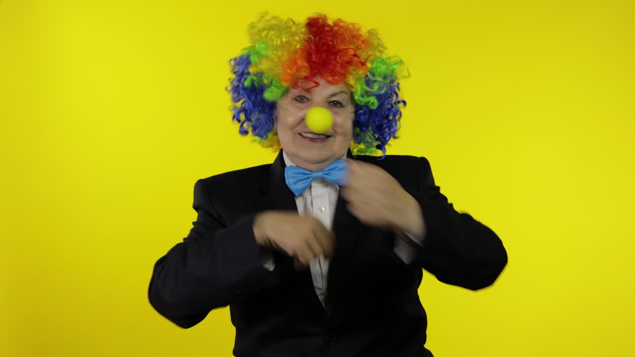 anciana payasa en peluca divirtiéndose, sonriendo, bailando, haciendo caras tontas