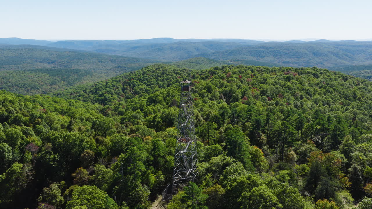 Torre di osservazione antincendio Devils Knob sopra una fitta foresta verde, circondata da colline e montagne in Arkansas. Ripresa orbitante con drone
