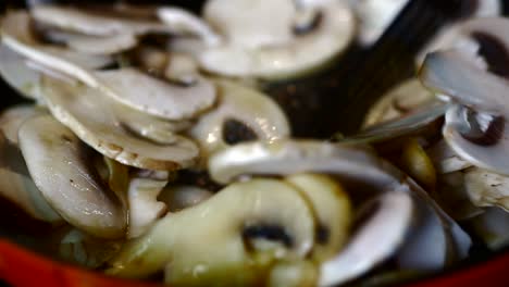 los champiñones en rodajas se fríen en una sartén roja caliente