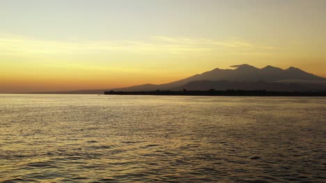 sunset-over-the-ocean-and-island-with-mountain,-Golden-horizon-and-calm-sea-landscape