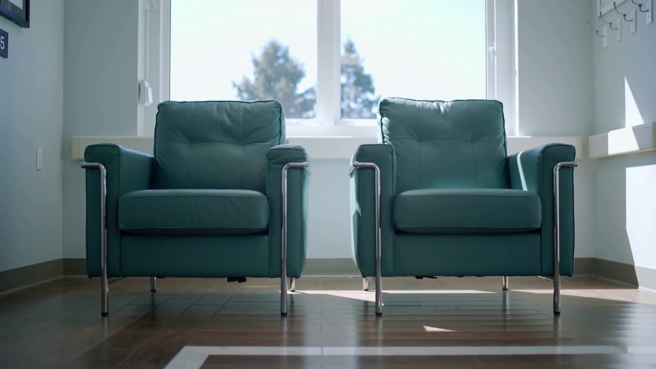 Moving camera framing two teal armchairs in clinic lobby, zooming in showing chrome legs, sunlight