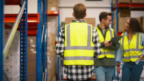 male and female workers with digital tablet walking between shelves in busy warehouse