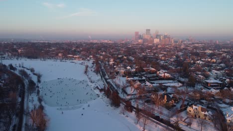 drone over skaters on lake of the isles approaching downtown minneapolis, mn during winter golden hour