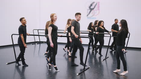 male and female students at performing arts school rehearsing ballet in dance studio using barre