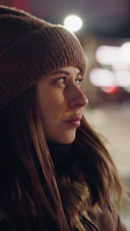 vista en primera persona de una mujer con un abrigo de invierno con una capucha de piel, caminando por una carretera por la noche. el aire frío está visiblemente saliendo de su boca, y el fondo presenta luces borrosas de la ciudad