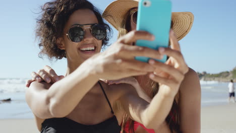 two girl friends taking selfies giving kiss on cheek on the beach